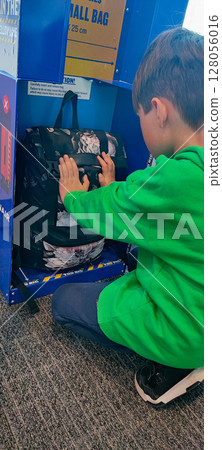 A young boy in a green sweatshirt is checking if a backpack fits into a Ryanair small cabin bag sizer at the airport. the travel preparation process, specifically budget airline luggage policies. 128056016