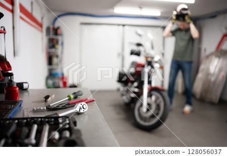 Man In Garage With Classic Motorcycle Wearing Protective Helmet 128056037