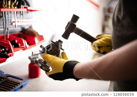 Serviceman Repairing An Auto Part With A Hammer At The Workbench In Service 128056039