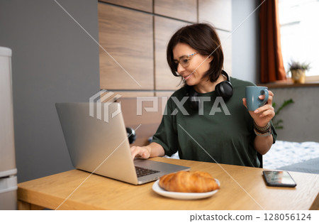 Freelance Girl Working At Home On A Computer While Having Breakfast In The Kitchen 128056124