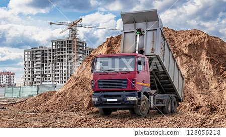 Construction site with dump truck unloading dirt near building under construction Construction site with dump truck unloading dirt near building under construction 128056218