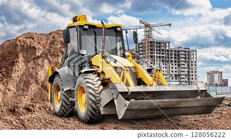 Excavator working on construction site with building and clouds in the background Excavator working on construction site with building and clouds in the background 128056222