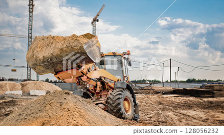 Construction vehicle lifts sand at a building site under a clear blue sky Construction vehicle lifts sand at a building site under a clear blue sky 128056232