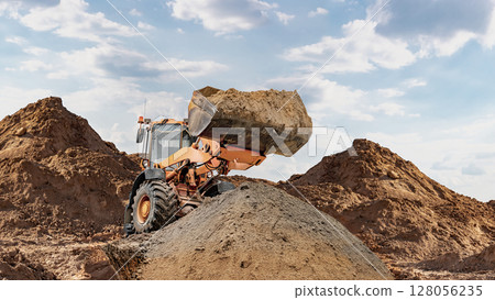 Heavy machinery moves earth at construction site under blue sky with clouds 128056235