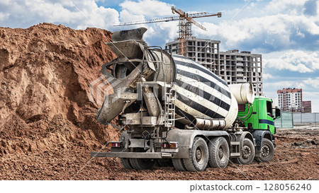 Cement mixer truck working at a construction site with a building under construction and earth mound in the background Cement mixer truck working at a construction site with a building under construction and earth mound in the background 128056240