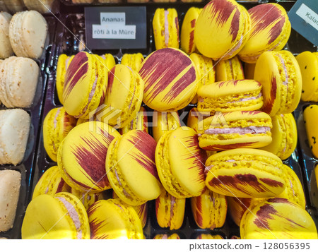 Colorful yellow macarons with vibrant red streaks are displayed together in a French pastry shop 128056395