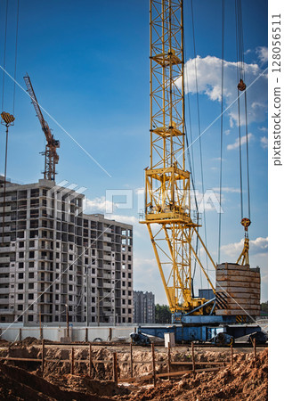 Construction site with a yellow crane lifting materials on a clear day in an urban area Construction site with a yellow crane lifting materials on a clear day in an urban area 128056511