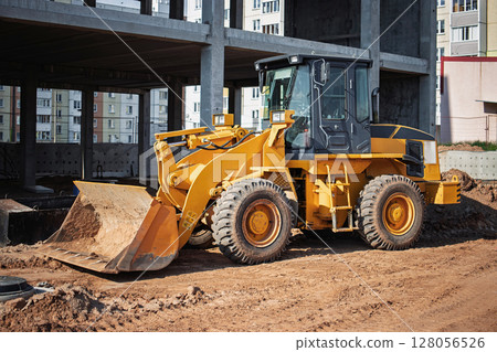 Construction site activity with a yellow loader parked near a newly built structure 128056526