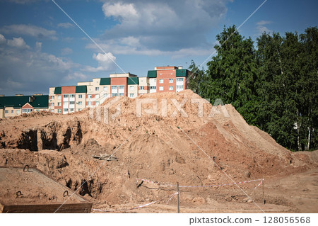 Construction site with earth mound and residential buildings under bright blue sky in mid-afternoon Construction site with earth mound and residential buildings under bright blue sky in mid-afternoon 128056568