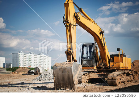 Excavator working on construction site in urban area under blue sky and fluffy clouds 128056580