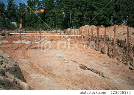 Construction site with freshly dug foundation surrounded by wooden supports and sand on a sunny day 128056583