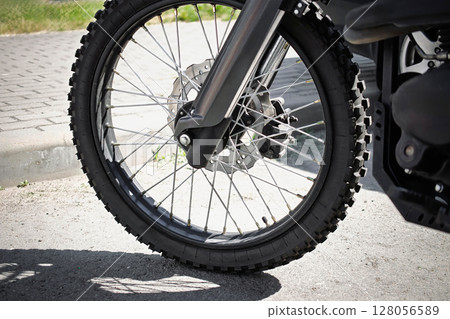 Close-up of a motorcycle front wheel on a sunny day in a parking area 128056589