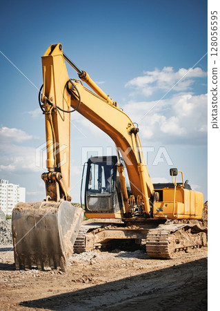 Heavy machinery excavator working on construction site under clear blue sky in urban area Heavy machinery excavator working on construction site under clear blue sky in urban area 128056595