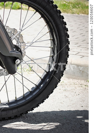Close-up of a motorcycle wheel with dirt tire on a sunny day near a paved road 128056607