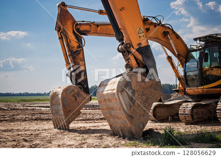 Heavy machinery working on construction site with a clear blue sky in the background during daylight hours 128056629