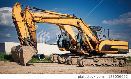Heavy machinery excavator working on construction site during sunny day with clouds 128056632