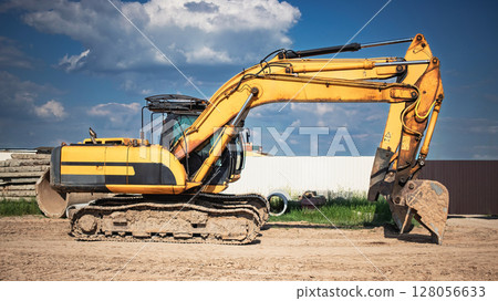 Heavy yellow excavator working on a construction site under a clear blue sky Heavy yellow excavator working on a construction site under a clear blue sky 128056633