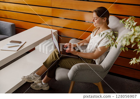 A Professional Woman Engaged in Working on a Laptop in a Stylish, Comfortable Living Space A Professional Woman Engaged in Working on a Laptop in a Stylish, Comfortable Living Space 128056907