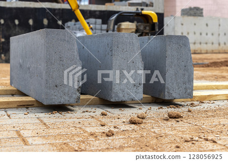 Roadside concrete curb stone with potholed road surface. Road repair work. Installation of a new curb stone before laying the new asphalt. 128056925