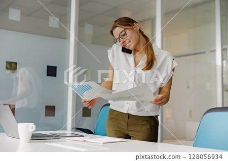 A Business Woman Actively Analyzing Important Documents in Her Modern Office Space 128056934
