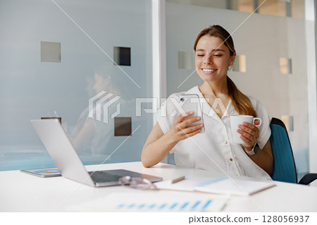 A young professional actively engaged in mobile communication while working at her desk A young professional actively engaged in mobile communication while working at her desk 128056937