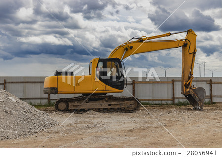 Backlit excavator on an industrial site against the background of the evening sky. Construction machinery for earthworks. Backlit excavator on an industrial site against the background of the evening sky. Construction machinery for earthworks. 128056941