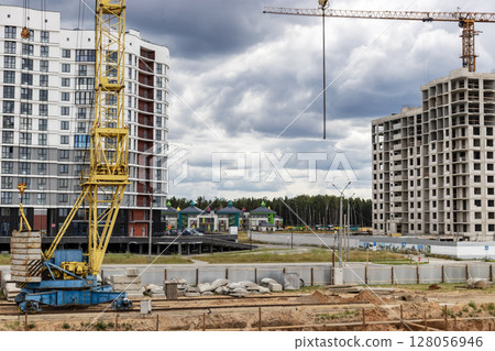 A large tower crane at a construction site against the backdrop of a modern monolithic house. Modern housing construction. industrial engineering. Construction of mortgage housing. A large tower crane at a construction site against the backdrop of a modern monolithic house. Modern housing construction. industrial engineering. Construction of mortgage housing. 128056946