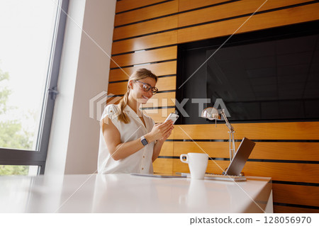 Woman Utilizing Smartphone Within a Contemporary and Modern Workspace for Efficiency and Creativity 128056970