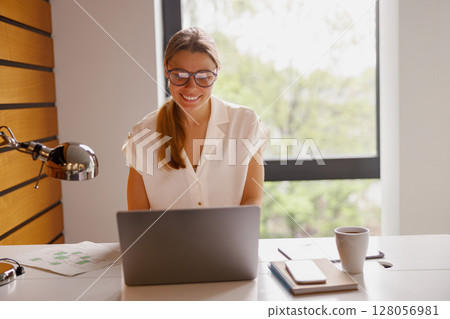 A Young Woman is Actively Working on Her Laptop in a Contemporary and Modern Workspace A Young Woman is Actively Working on Her Laptop in a Contemporary and Modern Workspace 128056981