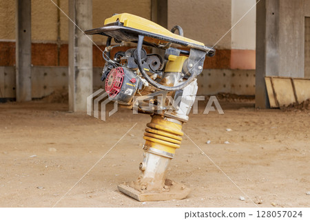 Vibratory rammer with vibrating plate on a construction site. Compaction of the soil before laying paving slabs. Close-up. Vibratory rammer with vibrating plate on a construction site. Compaction of the soil before laying paving slabs. Close-up. 128057024
