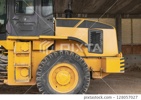 Heavy wheel loader with a bucket at a construction site. Close-up. Equipment for earthworks, transportation and loading of bulk materials - earth, sand, crushed stone. 128057027