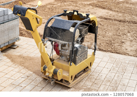 Vibratory rammer with vibrating plate on a construction site. Compaction of the soil before laying paving slabs. Close-up. Vibratory rammer with vibrating plate on a construction site. Compaction of the soil before laying paving slabs. Close-up. 128057068