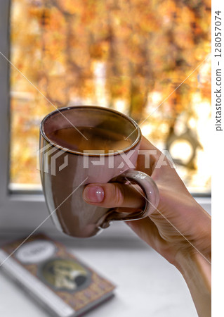 Cozy autumn moment with cup of coffee and book by window. Close-up Cozy autumn moment with cup of coffee and book by window. Close-up 128057074