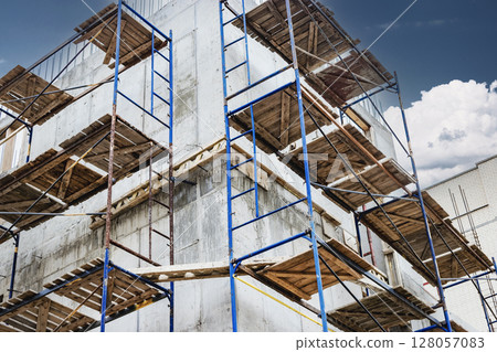Construction of a new monolithic reinforced concrete house. Scaffolding on the facade of a building under construction. Working at height on a construction site. 128057083