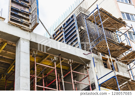 Construction of a new monolithic reinforced concrete house. Scaffolding on the facade of a building under construction. Working at height on a construction site. 128057085