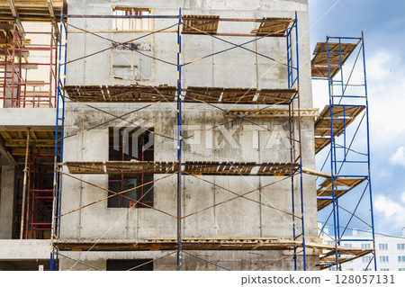 Construction of a new monolithic reinforced concrete house. Scaffolding on the facade of a building under construction. Working at height on a construction site. 128057131