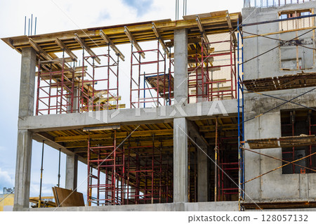 Construction of a new monolithic reinforced concrete house. Scaffolding on the facade of a building under construction. Working at height on a construction site. 128057132