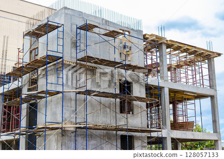 Construction of a new monolithic reinforced concrete house. Scaffolding on the facade of a building under construction. Working at height on a construction site. 128057133