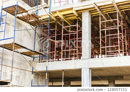 Construction of a new monolithic reinforced concrete house. Scaffolding on the facade of a building under construction. Working at height on a construction site. 128057151