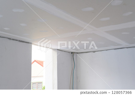 Interior renovation project building gypsum board ceiling plastering smooth edges with electrical wire installation detail. Ceiling construction progresses towards achieving smooth finish 128057366