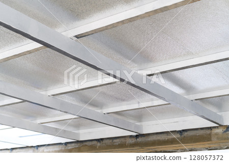 Close up view of ceiling structure with metal supports and insulating sheets. These panels likely contain pu foam for energy efficiency in construction. material forms protective layer Close up view of ceiling structure with metal supports and insulating sheets. These panels likely contain pu foam for energy efficiency in construction. material forms protective layer 128057372