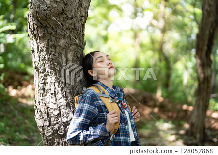 Relaxation in Nature. Young woman resting against a tree in a serene forest. 128057868