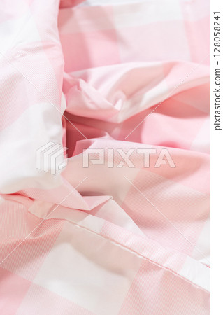 A pink and white checkered gingham fabric with gentle wrinkles and natural light. Highlights soft texture and pastel fabric color tones. A pink and white checkered gingham fabric with gentle wrinkles and natural light. Highlights soft texture and pastel fabric color tones. 128058241