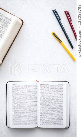 A book is open to a page with a pen and three pens on the table 128058798