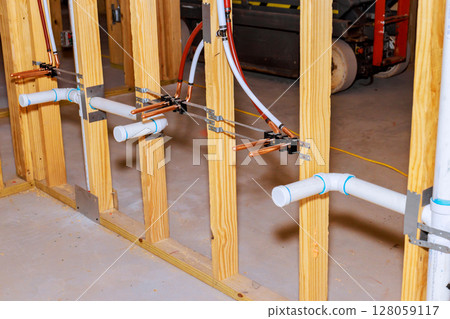 Copper, PVC pipes are being installed along wooden framing in basement, in plumbing setup process. Copper, PVC pipes are being installed along wooden framing in basement, in plumbing setup process. 128059117