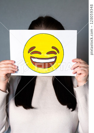 Woman holding happy smiling emoji mask in front of face. Social media trends, Gen Z marketing, World emoji day 17 July. Woman holding happy smiling emoji mask in front of face. Social media trends, Gen Z marketing, World emoji day 17 July. 128059348