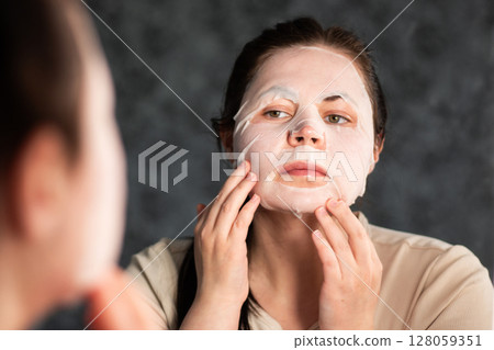 Side view of female carefully placing facial sheet mask. Useful for demonstrating proper skincare routine. Self care concept. 128059351