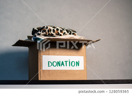 Cardboard box full of clothing ready for donation. Modern eco friendly habits and conscious consumption. Zero waste. Cardboard box full of clothing ready for donation. Modern eco friendly habits and conscious consumption. Zero waste. 128059365