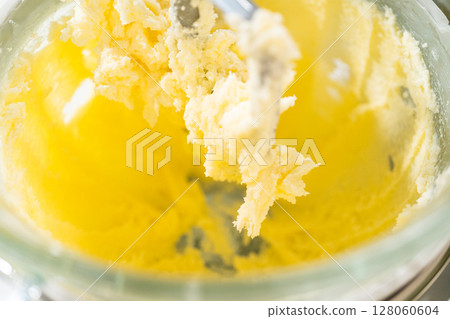 Close-up view of a mixer combining butter, sugar, and egg in the process of making Classic Sugar Cookie Dough. The partially mixed ingredients create a creamy texture as they blend together, forming 128060604