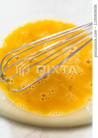 Close-up view of a whisk resting in a bowl of beaten eggs, prepared for Classic Sugar Cookie Dough. The eggs are well-mixed and slightly frothy, ready to be incorporated into the dough mixture as part Close-up view of a whisk resting in a bowl of beaten eggs, prepared for Classic Sugar Cookie Dough. The eggs are well-mixed and slightly frothy, ready to be incorporated into the dough mixture as part 128060606